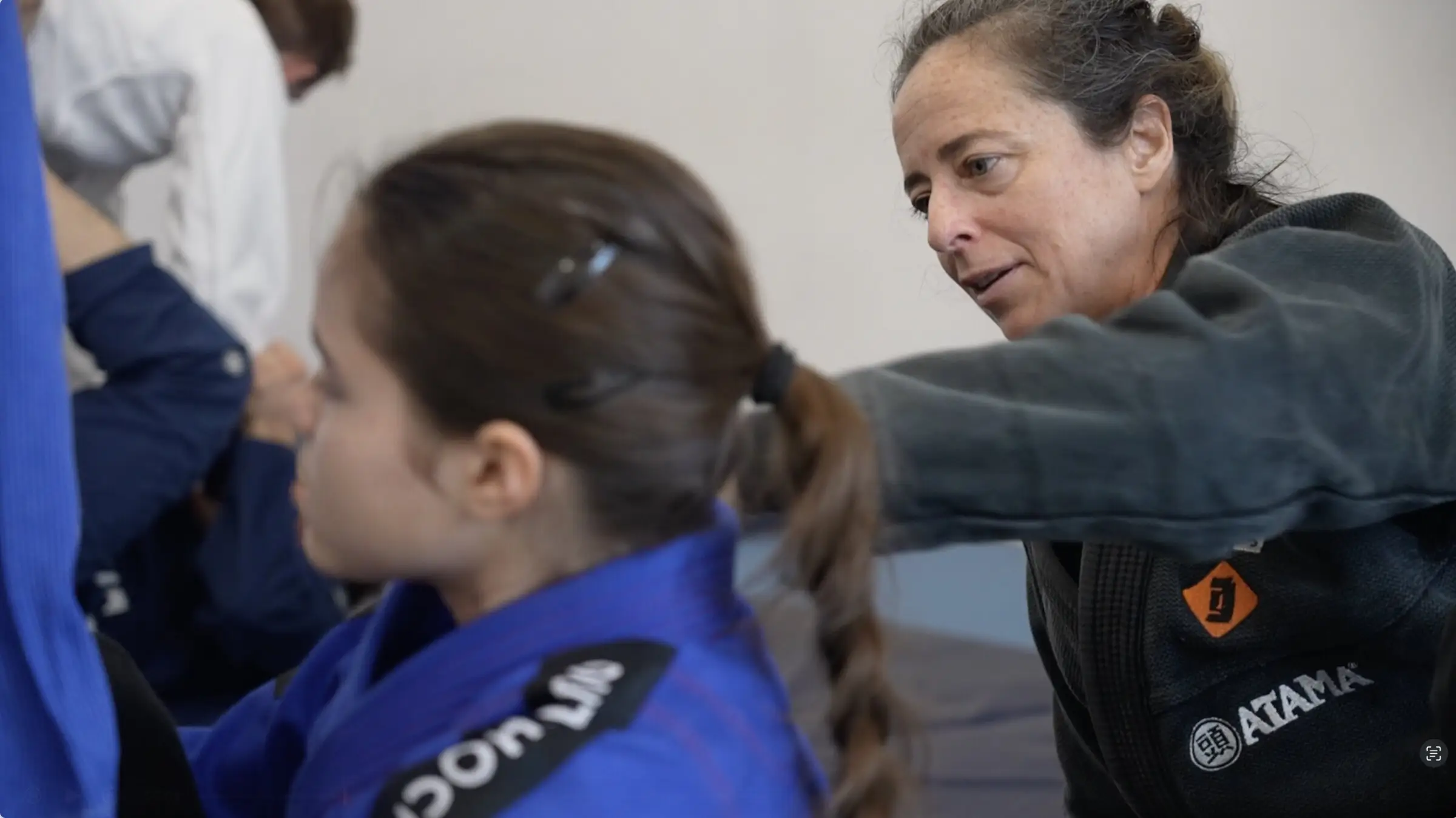 La professeure se penche vers une élève en kimono bleu pour corriger un placement