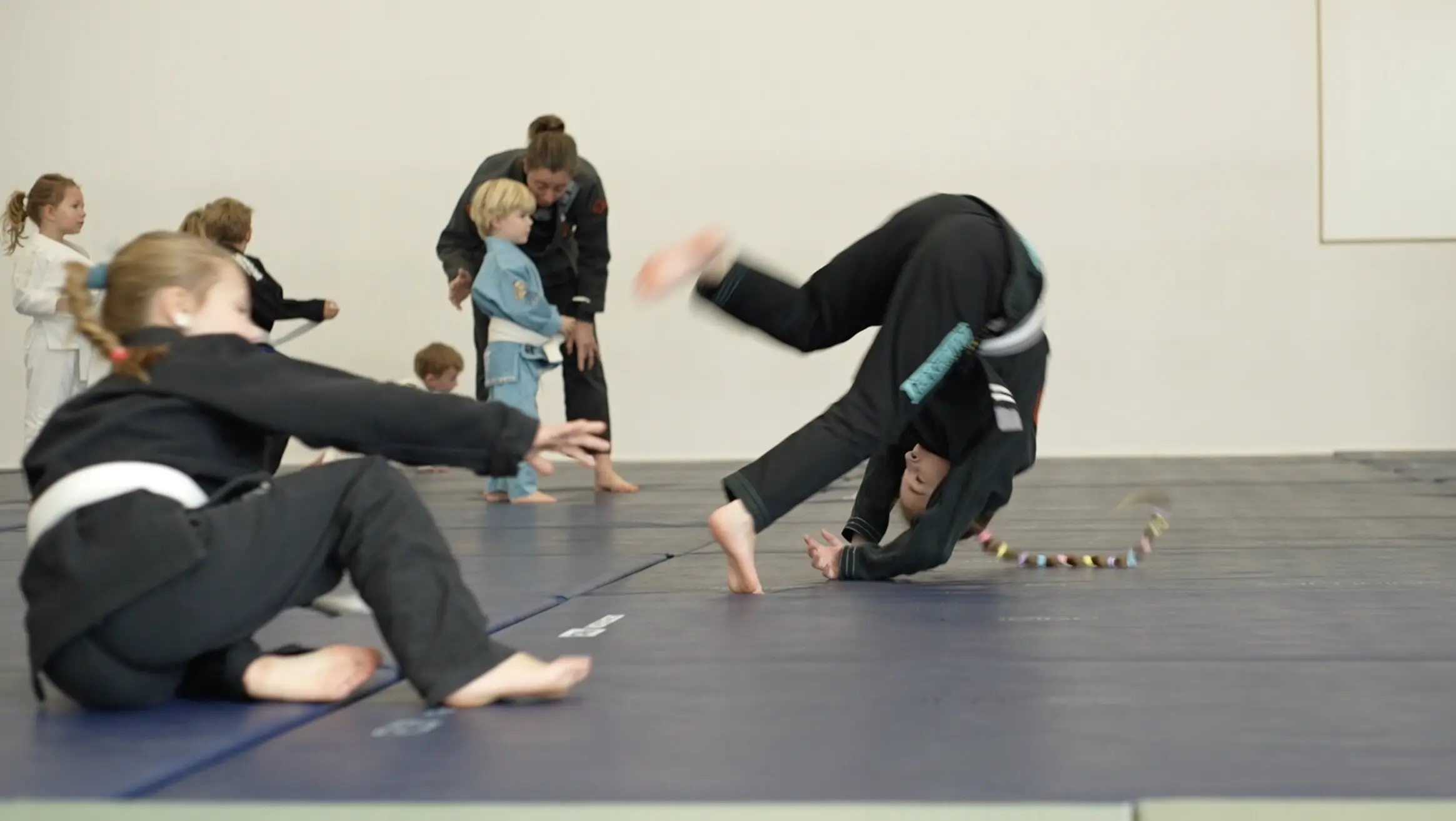 Des enfants enchaînent des roulades sur le tatami pendant un cours