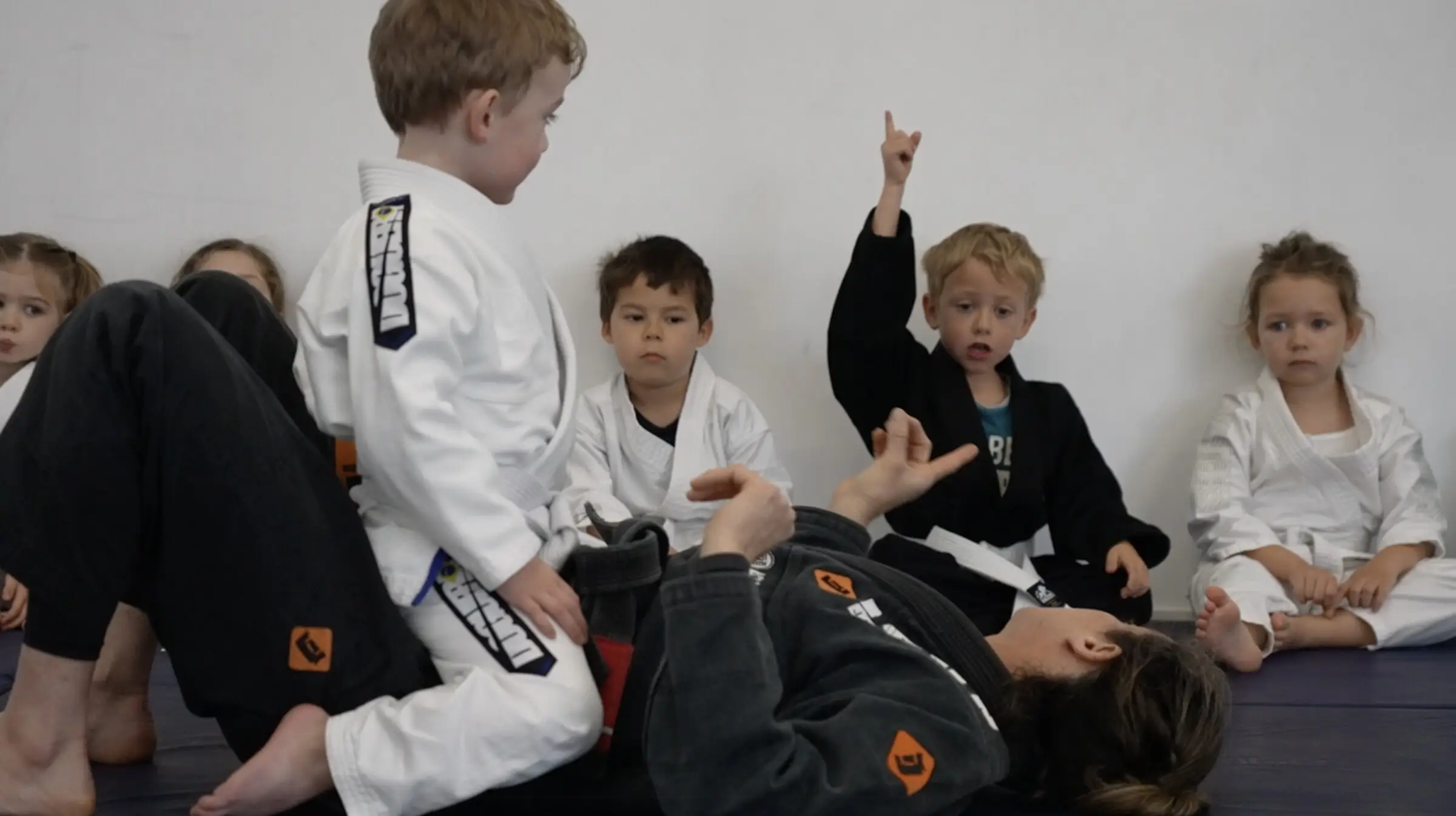 Des enfants assis en kimono regardent une démonstration au sol